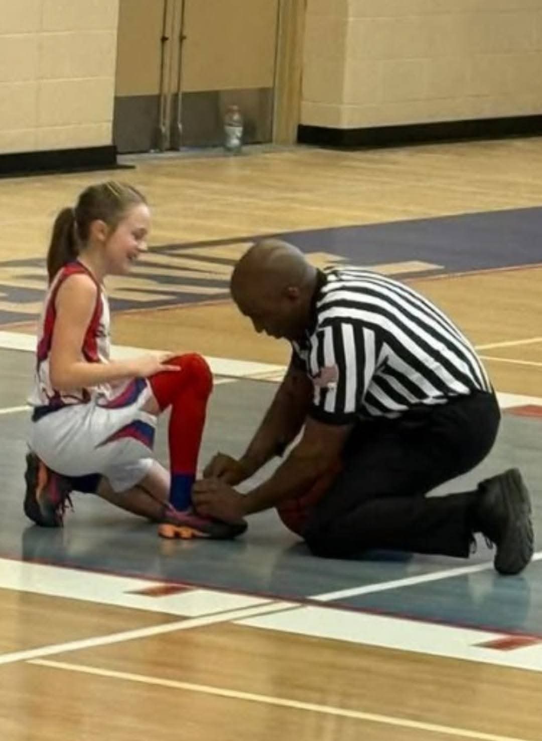 Wayne kneeling to tie a young player's shoe during a game
